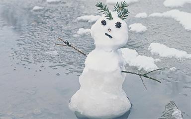 Small snowman melting on the sidewalk.